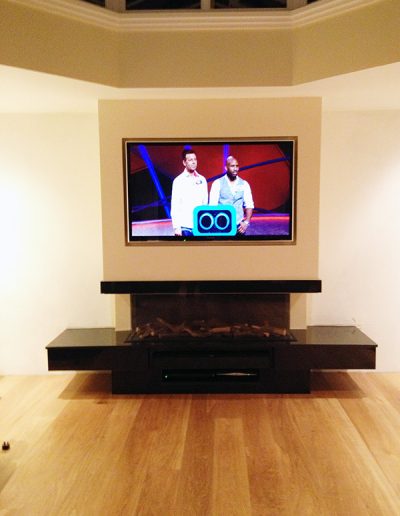 A contemporary black granite surround, fitted with a gas fire. We worked with media installation specialists to build this false chimney breast to accommodate both the unique fireplace and the TV system